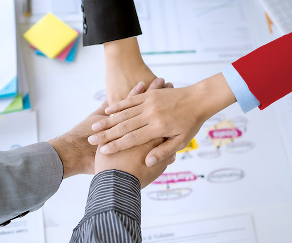 Four hands of people joined in a gesture of collaboration, on a desk with documents and colored post-its