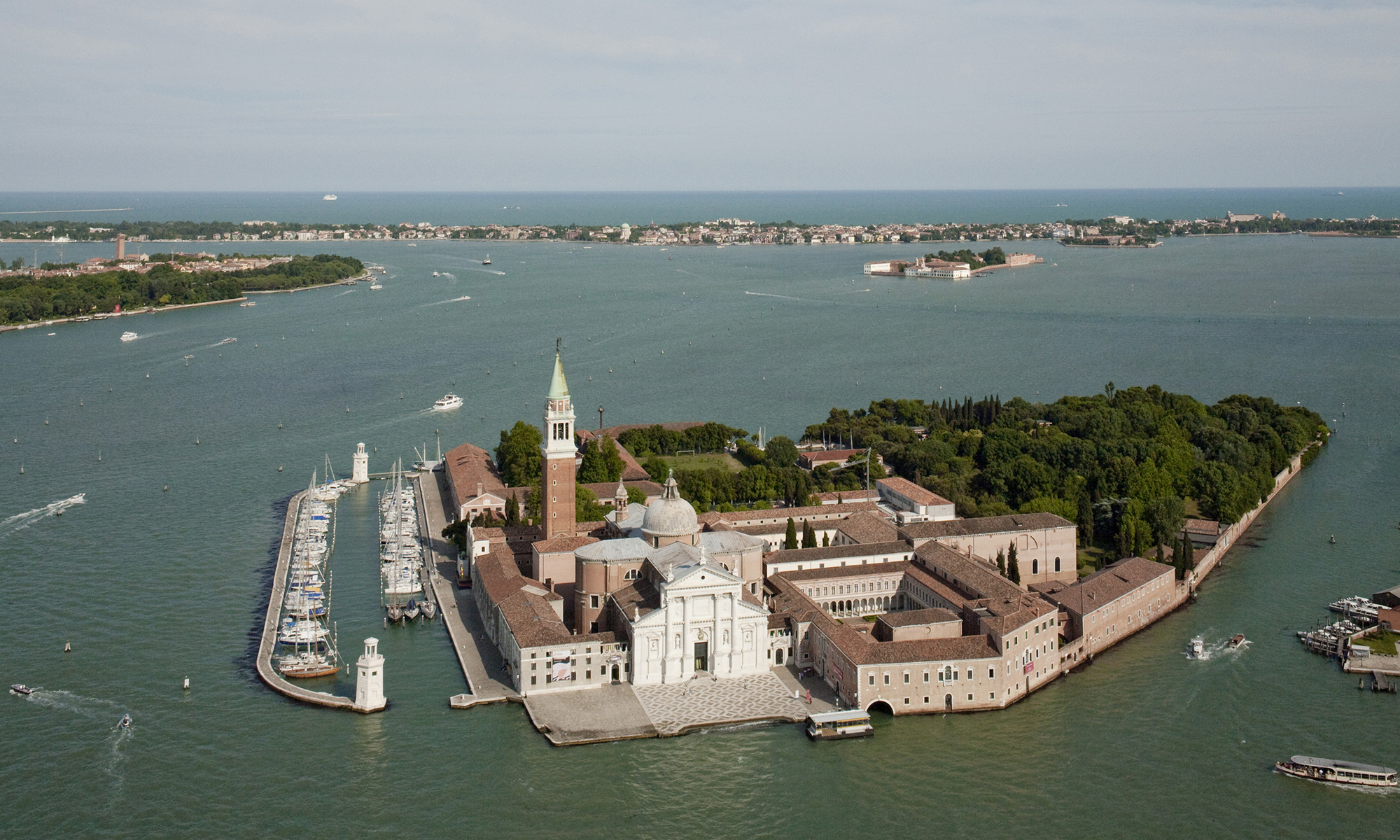 Aerial view of the Island of San Giorgio Maggiore in Venice, with the Basilica, the bell tower and the Giorgio Cini Foundation surrounded by the lagoon and boats moored in the port