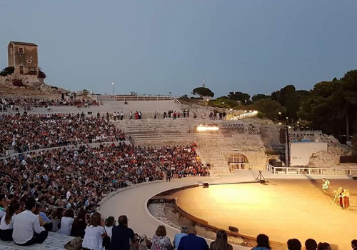 Evening show by the INDA Foundation at the Greek Theatre of Syracuse, with the audience sitting on the ancient steps and actors on stage illuminated by spotlights